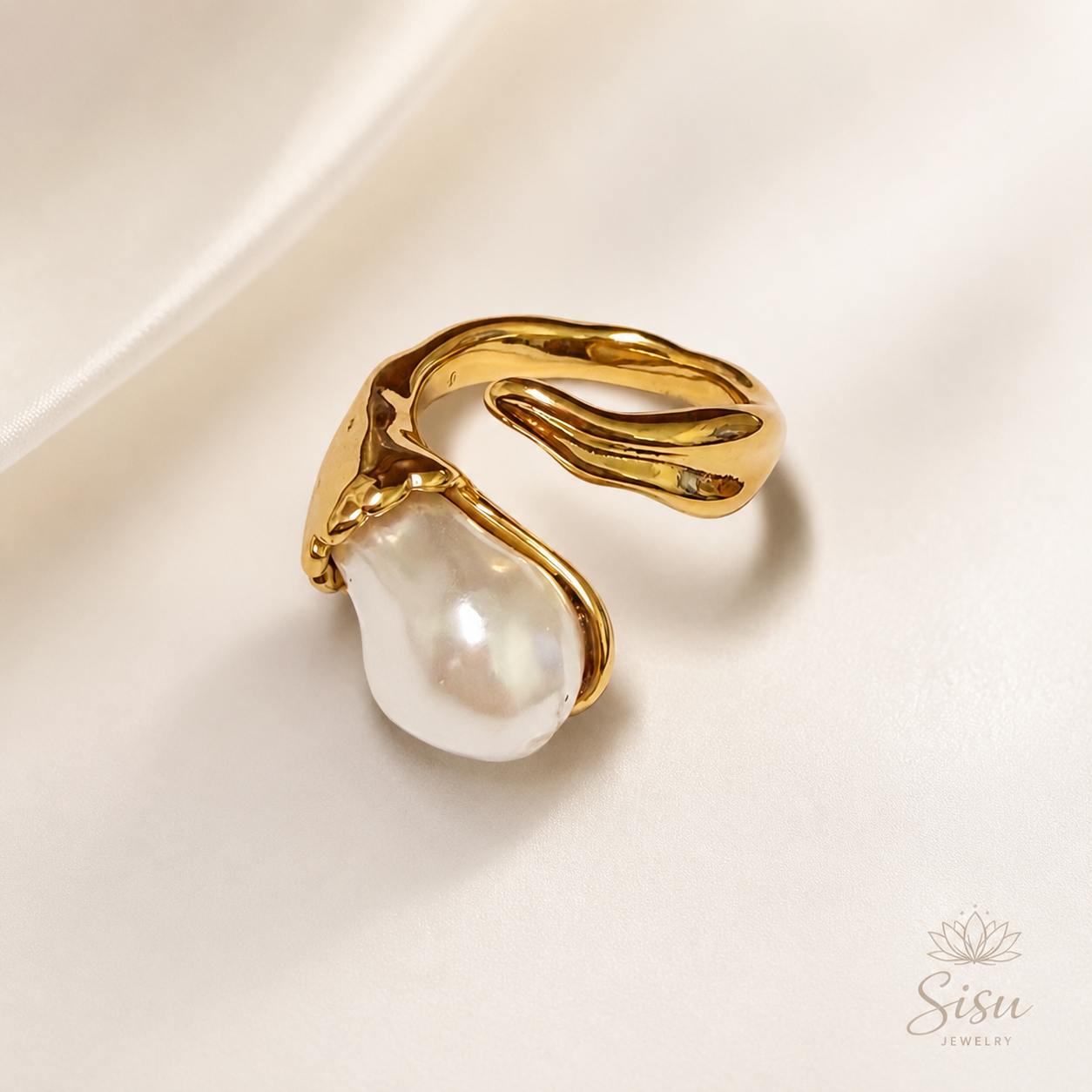 Anillo dorado de diseño orgánico con perla barroca sobre fondo crema elegante de Sisu Jewelry.