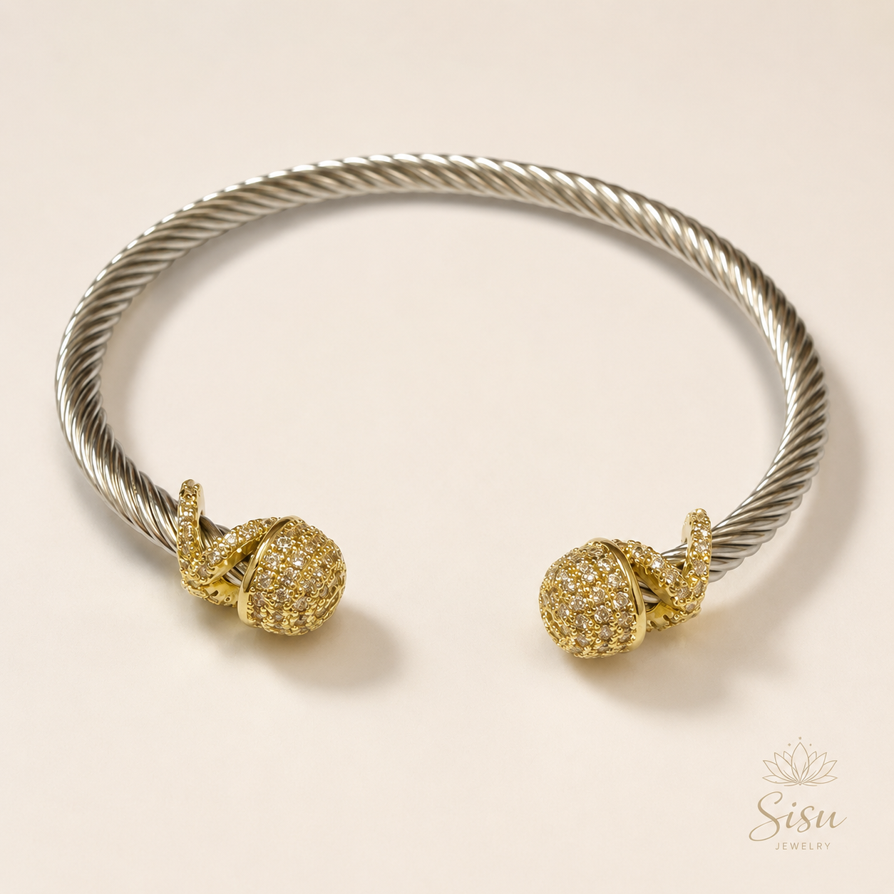 Brazalete plateado tipo cable con detalles dorados sobre fondo crema elegante de Sisu Jewelry.