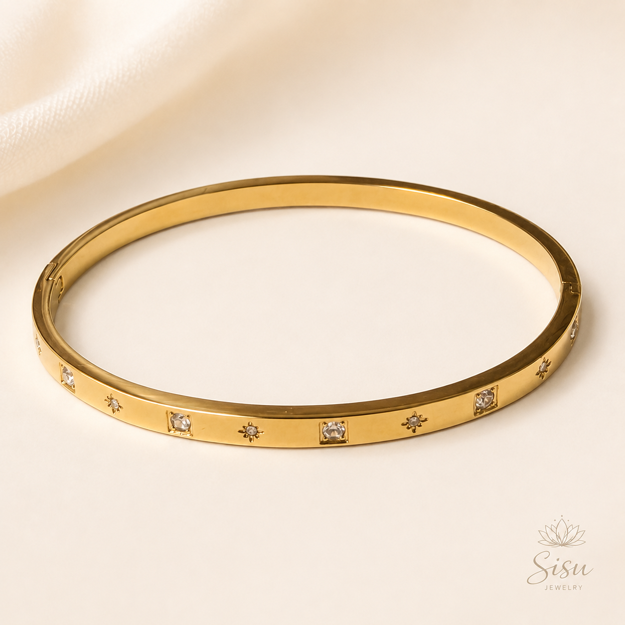 Brazalete dorado con detalles brillantes sobre fondo crema elegante de Sisu Jewelry.