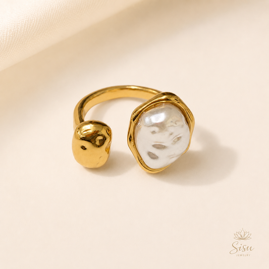 Anillo dorado abierto con perla irregular sobre fondo crema elegante de Sisu Jewelry.