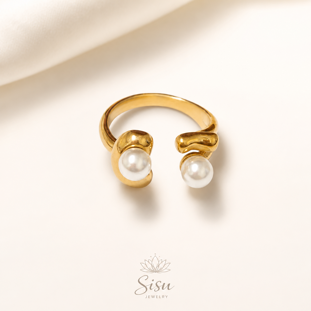 Anillo dorado abierto con dos perlas blancas sobre fondo crema elegante de Sisu Jewelry.