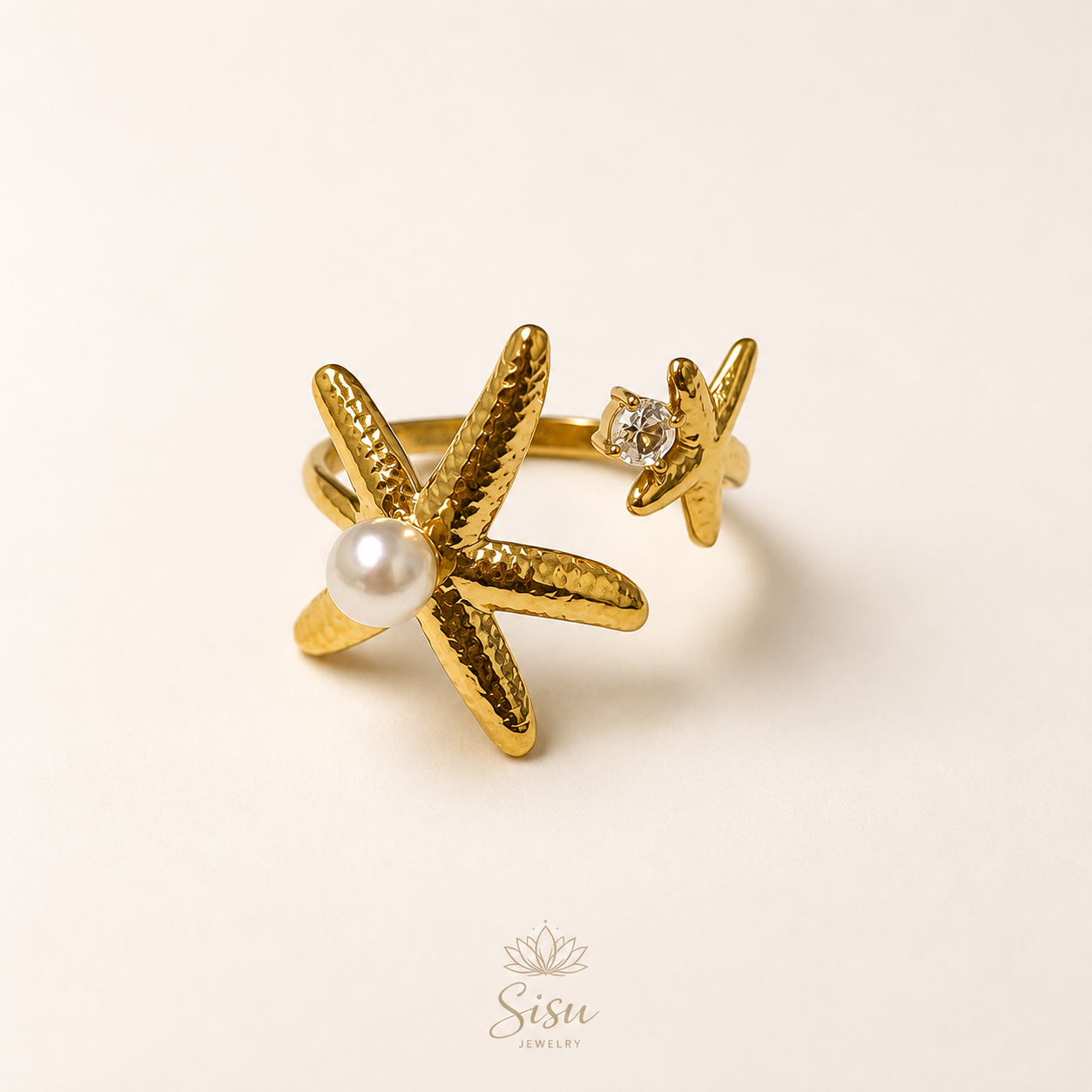 Anillo dorado con estrella de mar, perla y detalle brillante sobre fondo crema elegante de Sisu Jewelry.