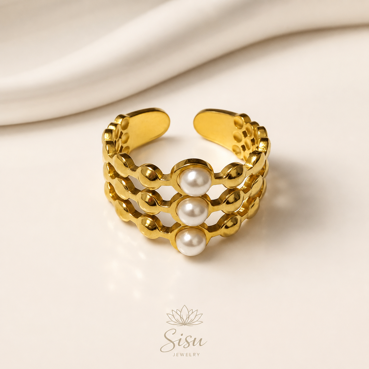 Anillo dorado tipo cuff con tres perlas blancas sobre fondo crema elegante de Sisu Jewelry.