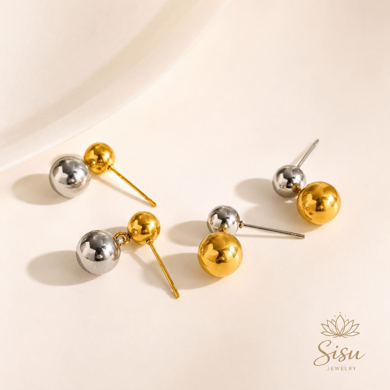 Aretes de esferas doradas y plateadas sobre fondo crema elegante de Sisu Jewelry.