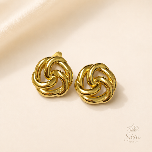 Aretes dorados en diseño de nudo sobre fondo crema elegante de Sisu Jewelry.