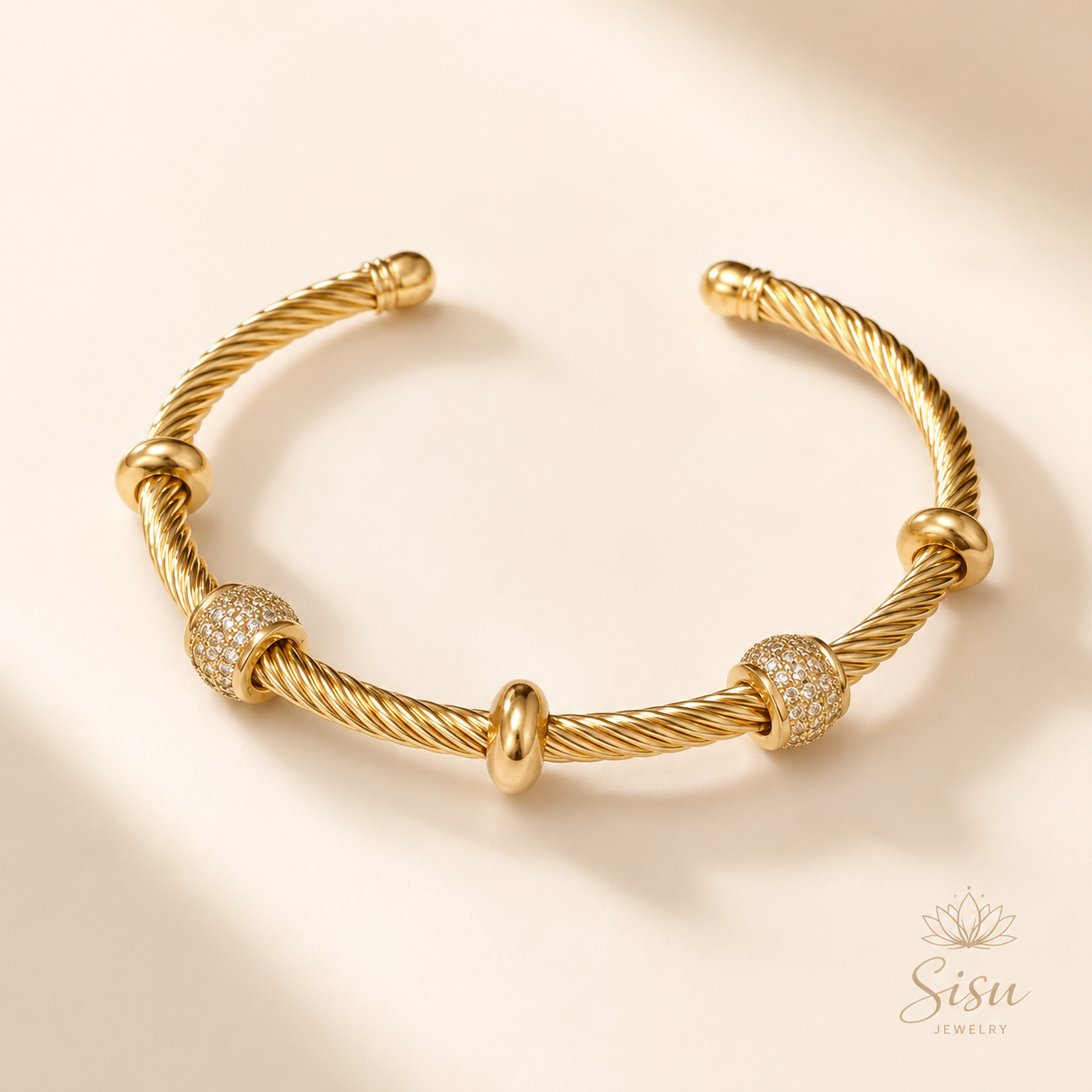 Brazalete dorado tipo cable con detalles decorativos sobre fondo crema elegante de Sisu Jewelry.