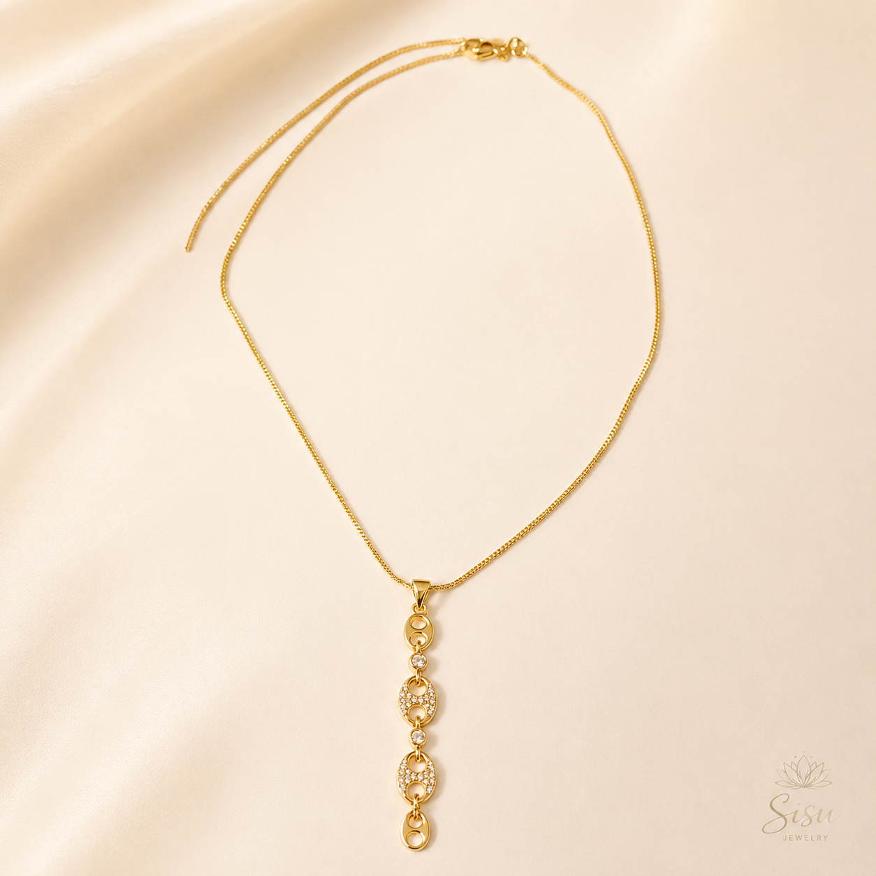 Collar dorado con colgante de eslabones brillantes sobre fondo crema elegante de Sisu Jewelry.