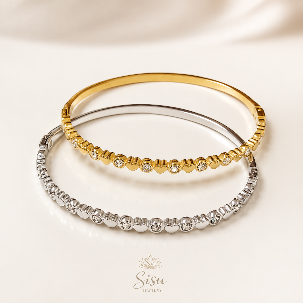 Bazaletes dorado y plateado con corazones sobre fondo crema elegante de Sisu Jewelry.