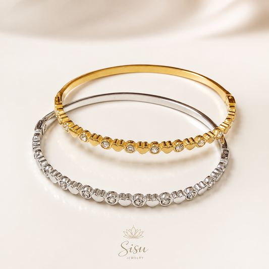 Bazaletes dorado y plateado con corazones sobre fondo crema elegante de Sisu Jewelry.