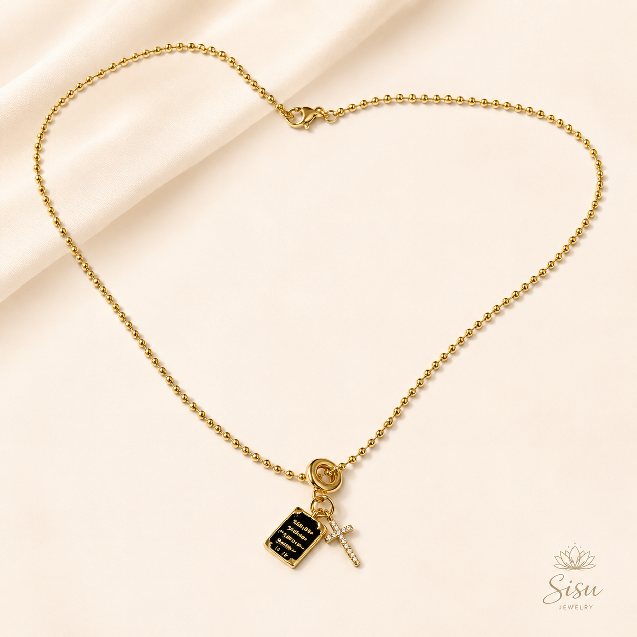 Collar dorado con charm de Biblia y cruz sobre fondo crema elegante de Sisu Jewelry.