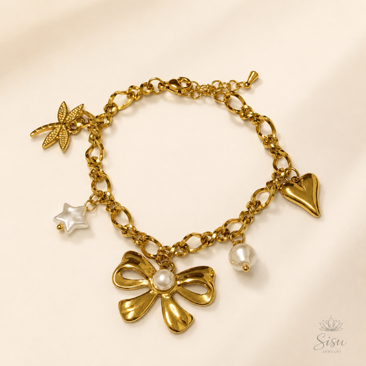 Pulsera dorada con charms, perlas y lazo sobre fondo crema elegante de Sisu Jewelry.